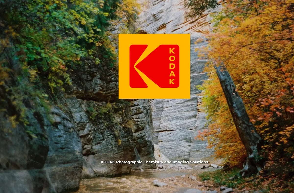 A Kodak logo overlay centered on a natural outdoor scene with rocky cliffs and autumn trees in green, yellow, and orange tones. Small Kodak text appears near the bottom.