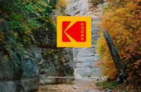 A Kodak logo overlay centered on a natural outdoor scene with rocky cliffs and autumn trees in green, yellow, and orange tones. Small Kodak text appears near the bottom.