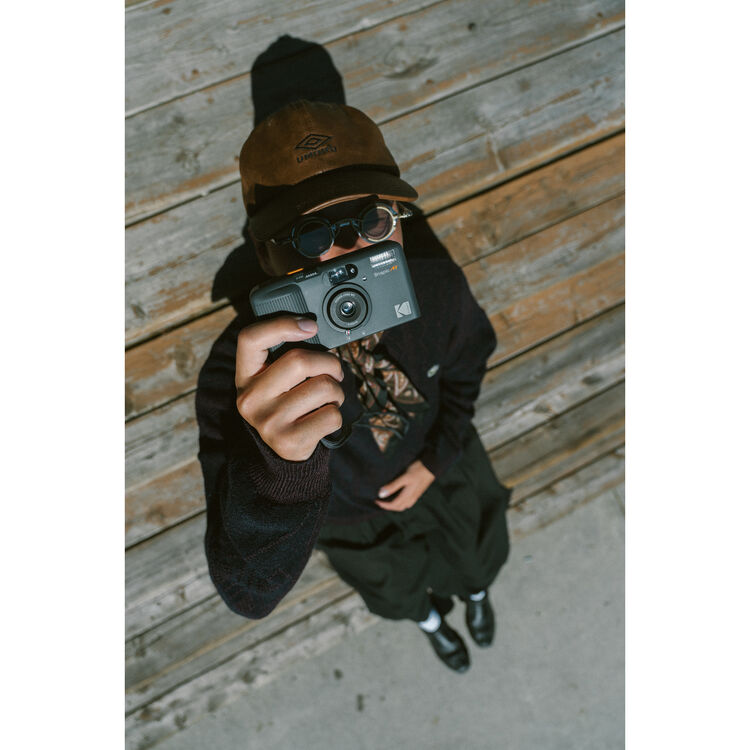 Snapic image of a person holding a camera against a wooden wall