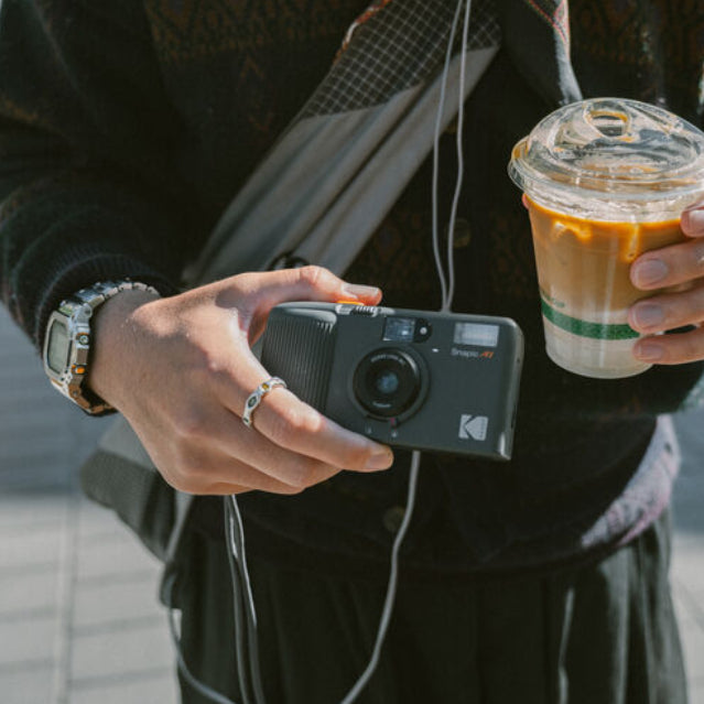 Person holding a camera and a coffee cup outdoors
