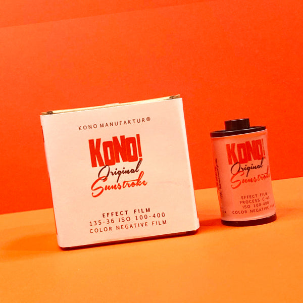 A vintage Kono Original Sunstroke effect film box and a roll of color negative film on an orange surface against an orange background.