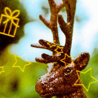 A close-up of a brown reindeer head with antlers, overlaid with yellow line drawings of stars, candy canes, and gift boxes against a blurred green and blue background.