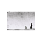 High-contrast black-and-white street photography showing a person walking past a large wall with a long cast shadow.