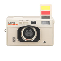 A retro-style beige compact camera by Lomo Apparatus, featuring a black lens housing, red brand lettering, and a yellow-and-red viewfinder window on a plain white background.