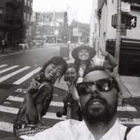 Black and white street selfie showing four people posing on a city crosswalk with buildings and street signs in the background.