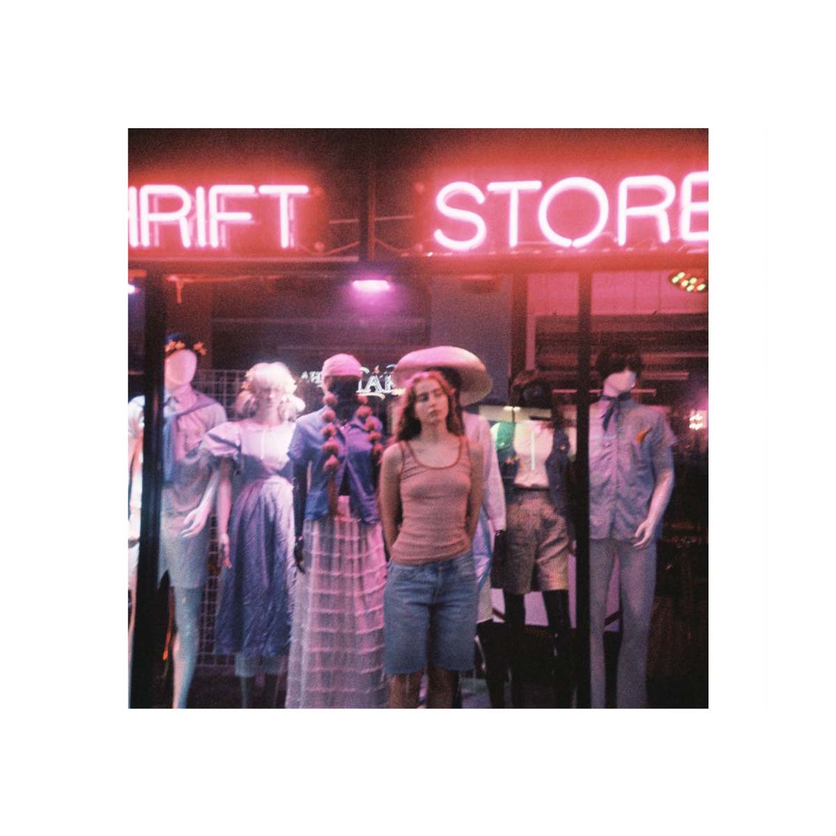 Album cover art for 'Drift Store' featuring a woman standing in front of a neon-lit storefront with mannequins dressed in clothing inside the shop.