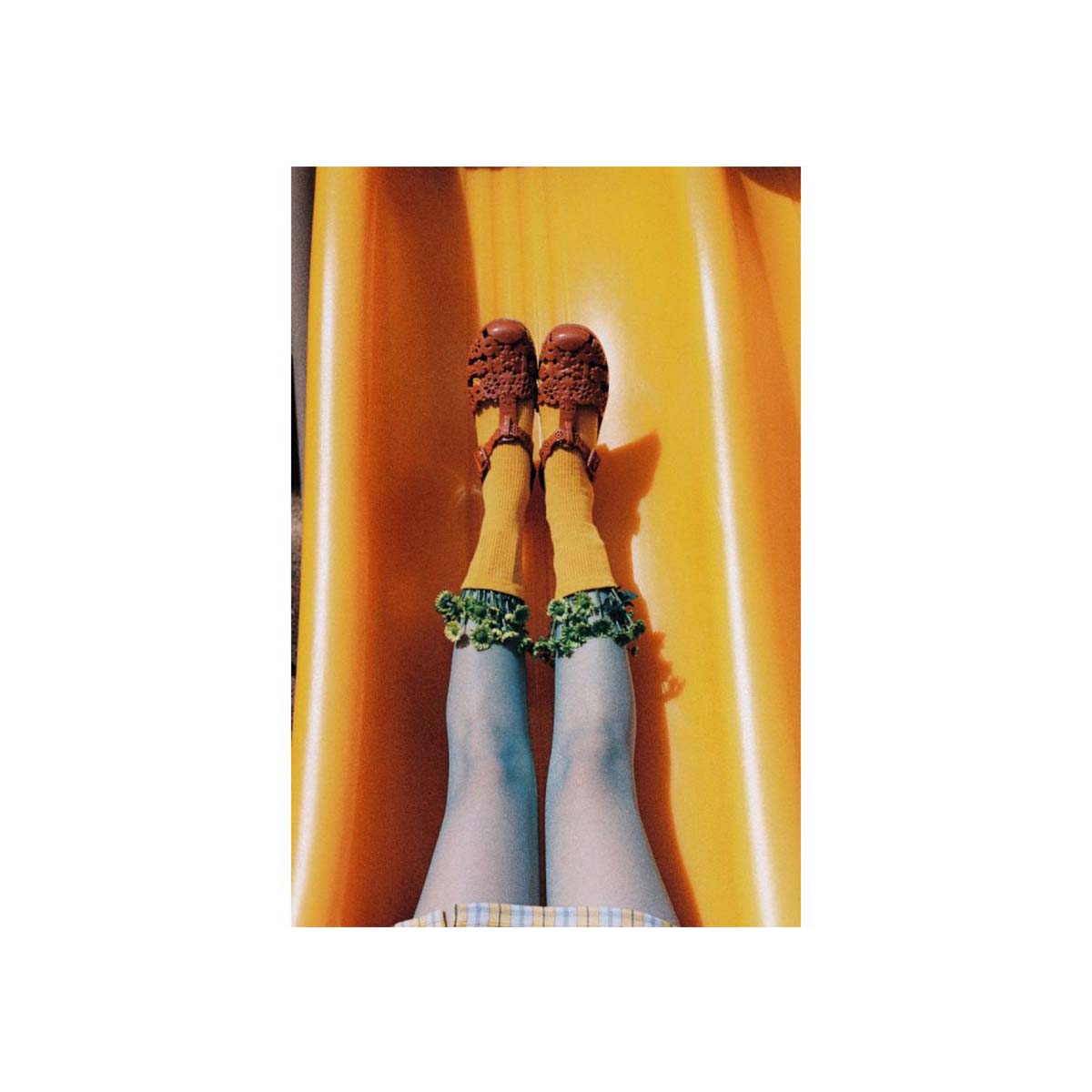 A top-down view of a person sliding down a bright yellow slide, wearing brown lace-up shoes, mustard yellow socks with green ruffled cuffs, and blue tights.
