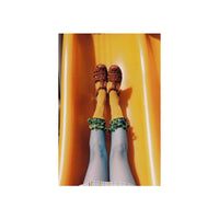 A top-down view of a person sliding down a bright yellow slide, wearing brown lace-up shoes, mustard yellow socks with green ruffled cuffs, and blue tights.