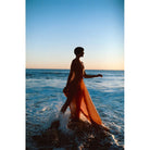 Silhouette of a person in a flowing orange dress walking through ocean waves at sunset, shot on LomoChrome Color '92 film.
