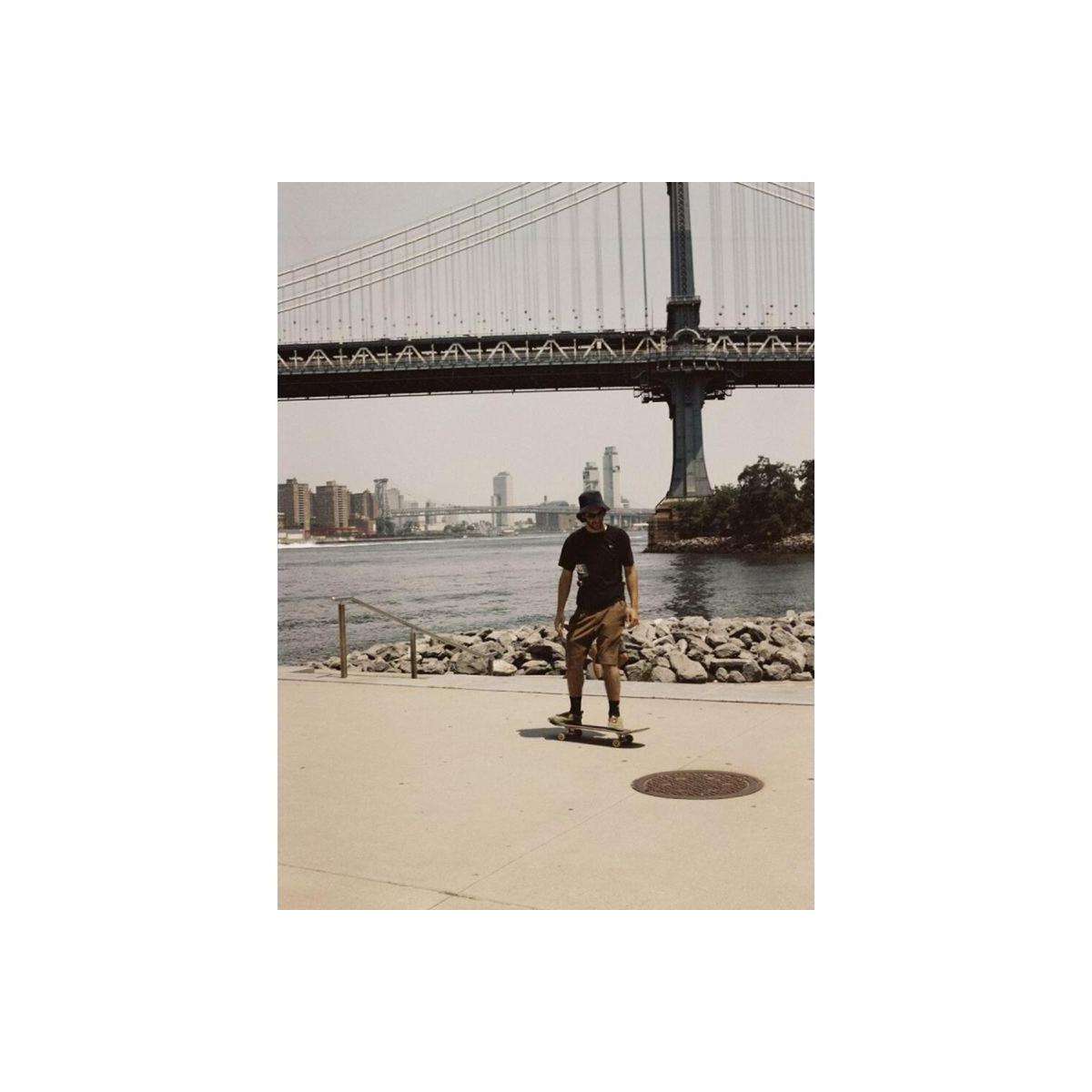 Skater on a waterfront path with a bridge in the background, captured in warm, vintage-toned 120 film style.