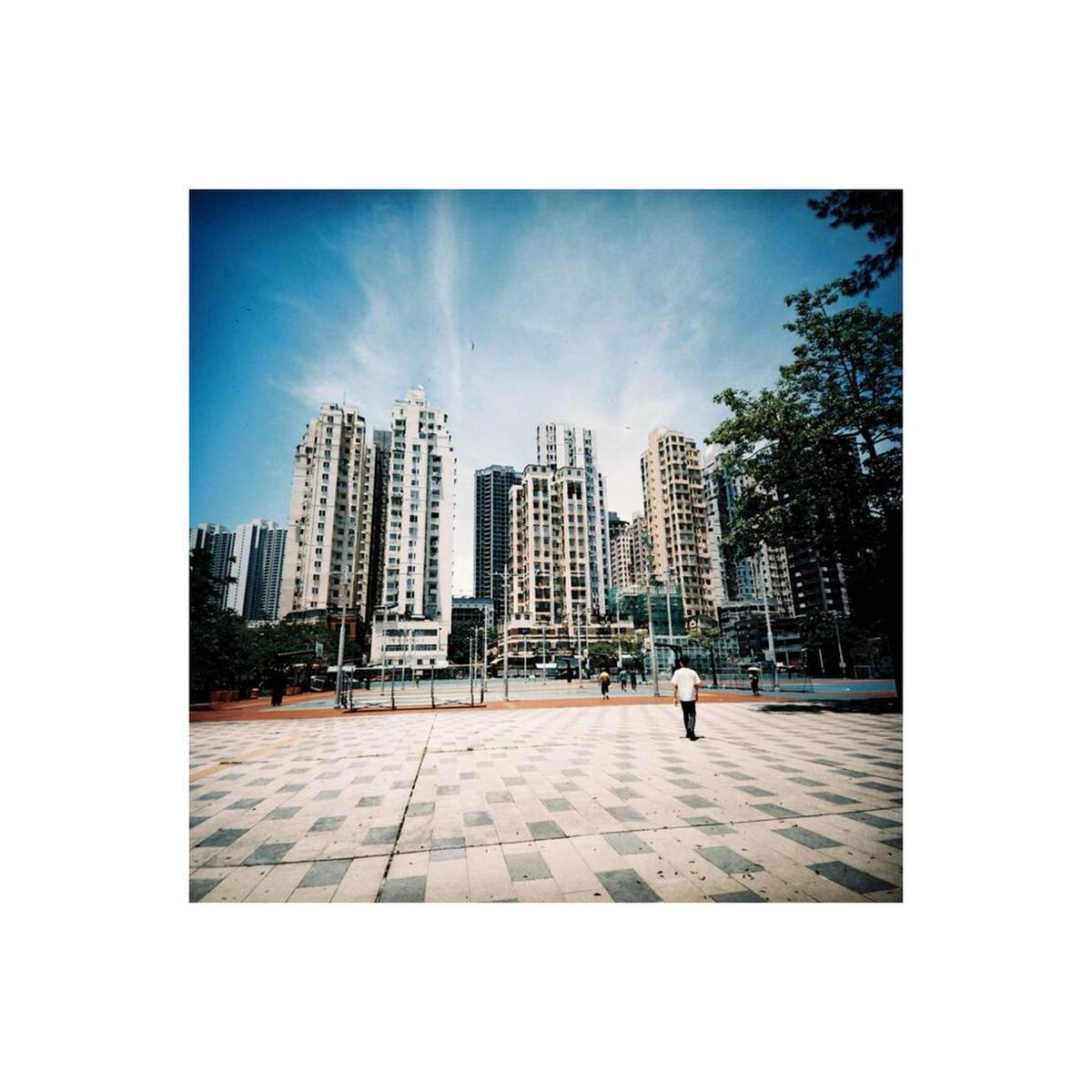 Medium-format film shot of a city plaza with tall apartment buildings, warm tones, and rich grain under a blue sky.