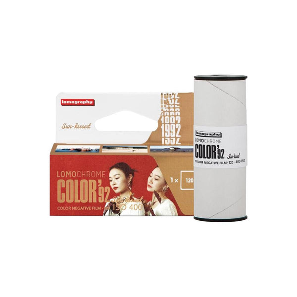 Lomography Color 32 film roll and its retail packaging, featuring a white spool with a black top and bottom and a cardboard-and-white box with red and brown panels and model imagery.