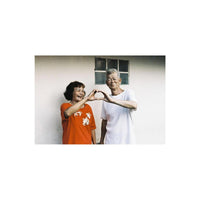 An elderly couple makes a heart shape with their hands, captured in the desaturated, gritty style of LomoChrome Metropolis.
