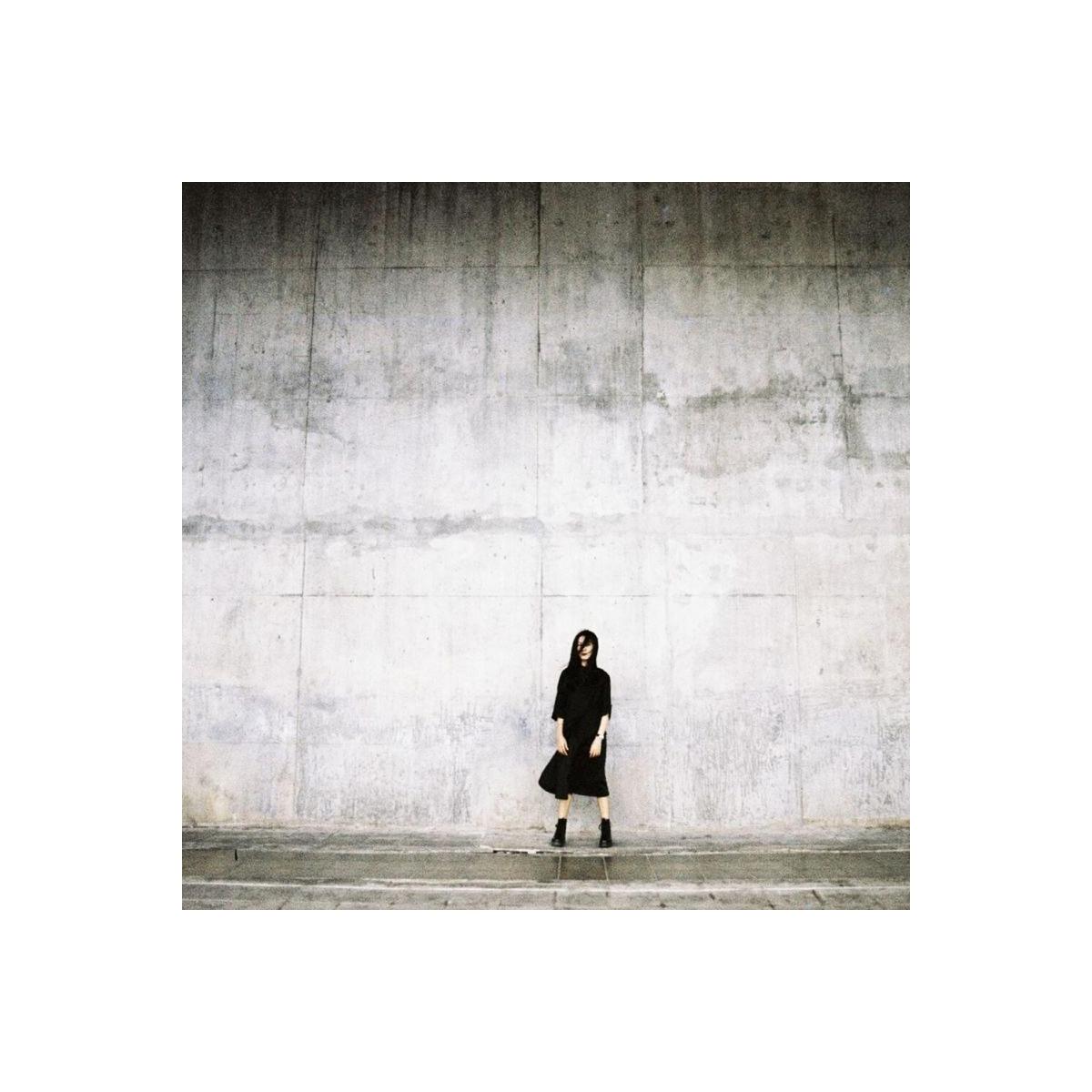 Person in black standing against a textured concrete wall, captured with the gritty, high-contrast look of LomoChrome film.
