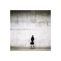 Person in black standing against a textured concrete wall, captured with the gritty, high-contrast look of LomoChrome film.