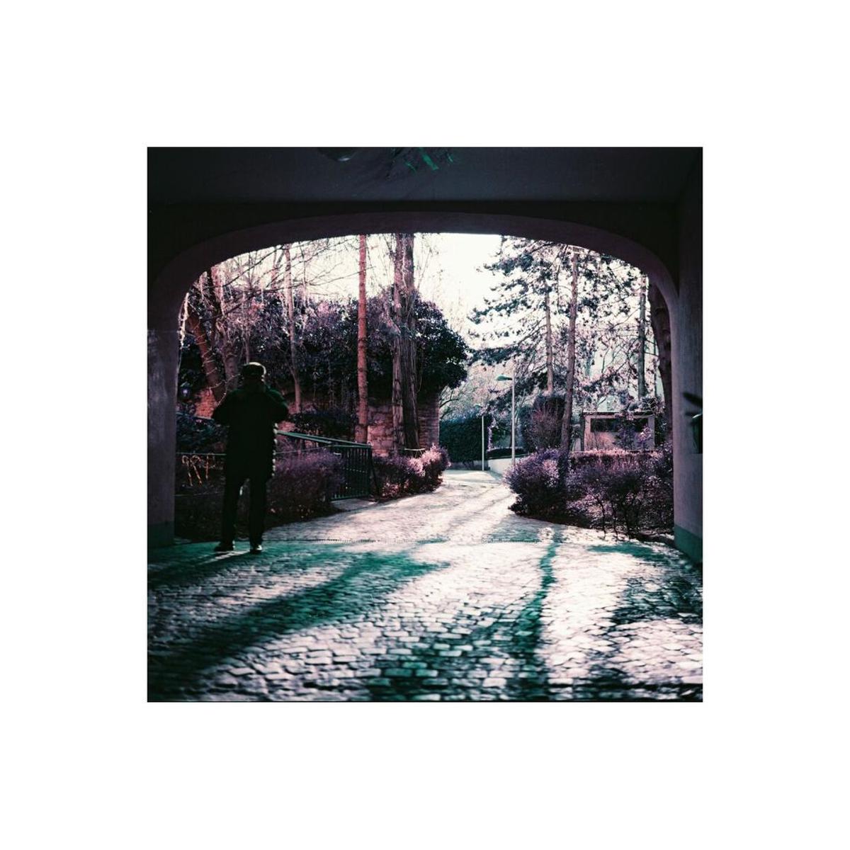 A person walking on a cobblestone path framed by an archway, captured in surreal purple and plum tones on 120 film.