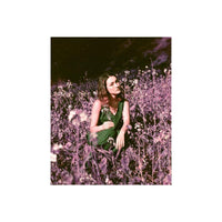 Woman in a green striped dress sitting in a field of surreal purple and pink flowers shot on LomoChrome 120 film.