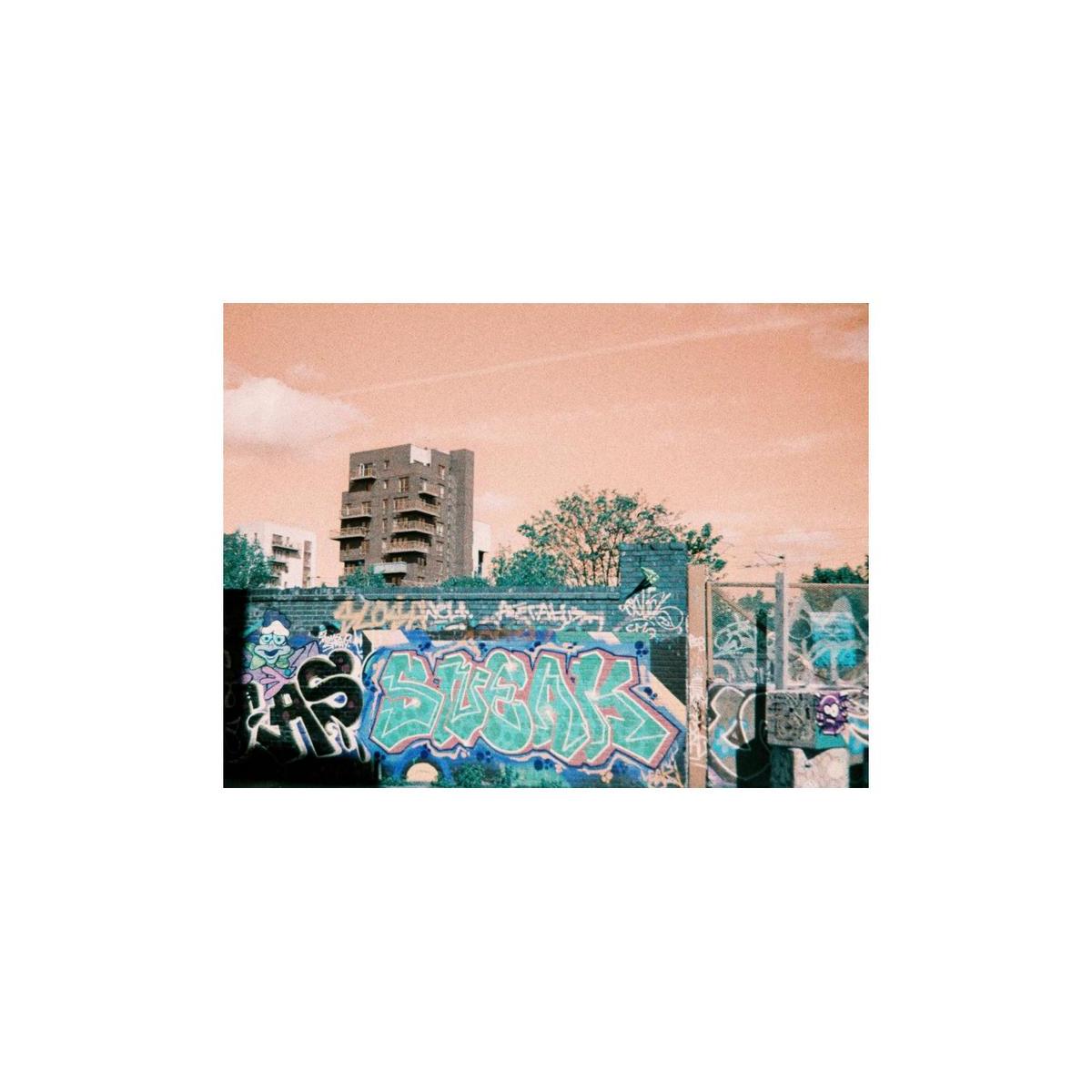 Urban graffiti wall with turquoise and blue color shifts against a peach-toned sky, captured on LomoChrome 110 film.