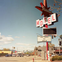 Vintage roadside motel sign reading 'Starburst Motel' with a large red star and white block letters, photographed outdoors on a street with cars, buildings, and a blue sky.