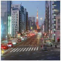 A scenic urban street in Tokyo at dusk, with tall buildings on both sides, cars with illuminated taillights on the road, and the Tokyo Tower visible in the distance against a blue evening sky.
