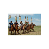 Group of Mongolian horsemen in traditional clothing carrying tall, feathered ceremonial poles across a sunny field.
