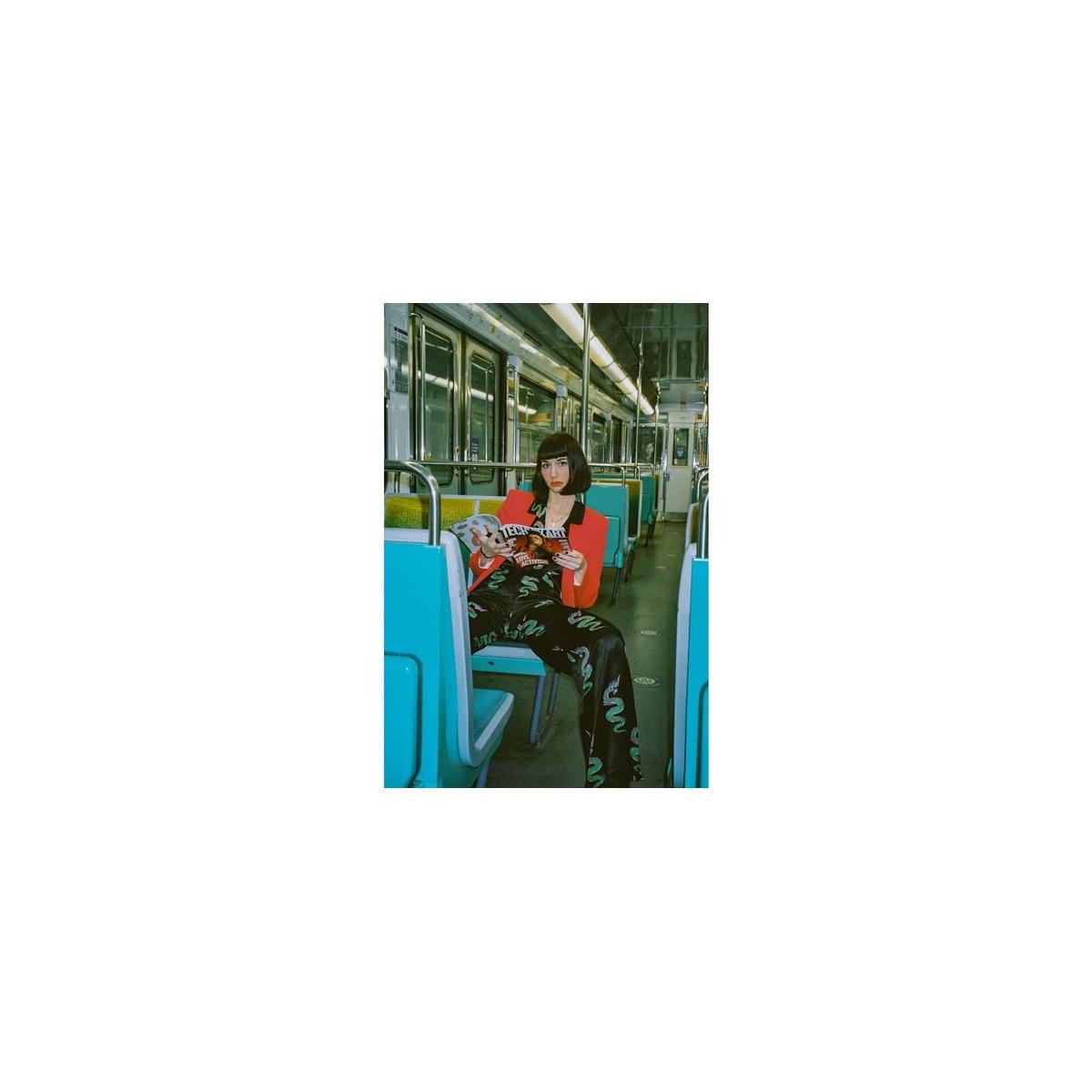 Person sitting on a train holding a dog, wearing a black outfit with green patterns.