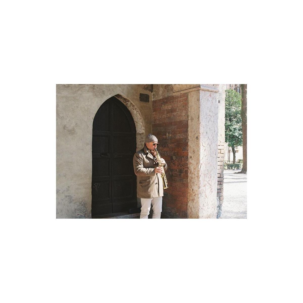 Person playing a saxophone against a stone building with an arched door.