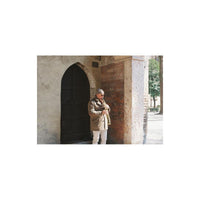 Person playing a saxophone against a stone building with an arched door.