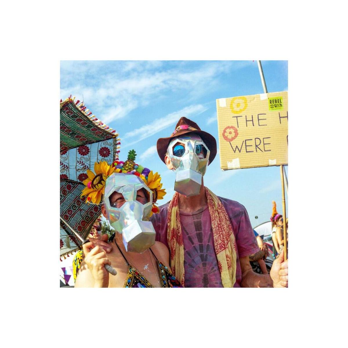 Two people wearing reflective geometric masks and festival attire under a bright blue sky, captured on Lomography 800 film.