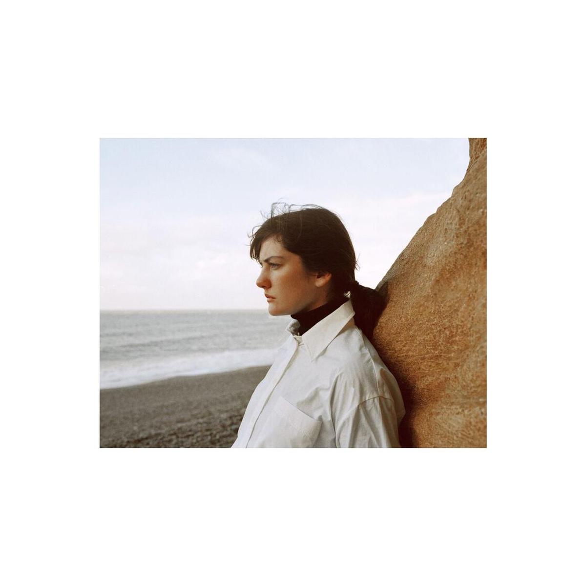 Portrait of a woman in a white shirt leaning against a rock on a beach, captured with Lomography 800 120 film.