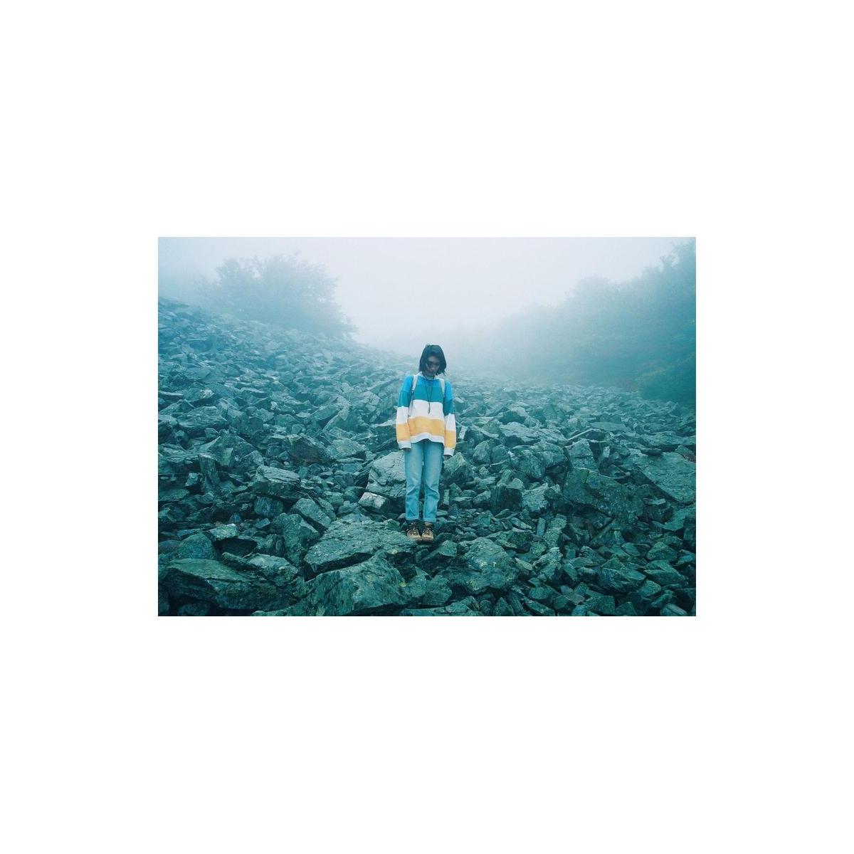 Person in a colorful sweater standing on a rocky, foggy hillside, captured with the grainy, saturated look of Lomography 800 film.