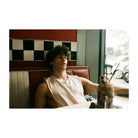 Young man sitting in a retro diner booth with red and white upholstery, captured with vintage analog film aesthetics.