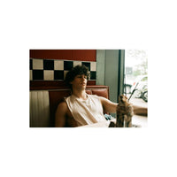 Young man sitting in a retro diner booth with red and white upholstery, captured with vintage analog film aesthetics.