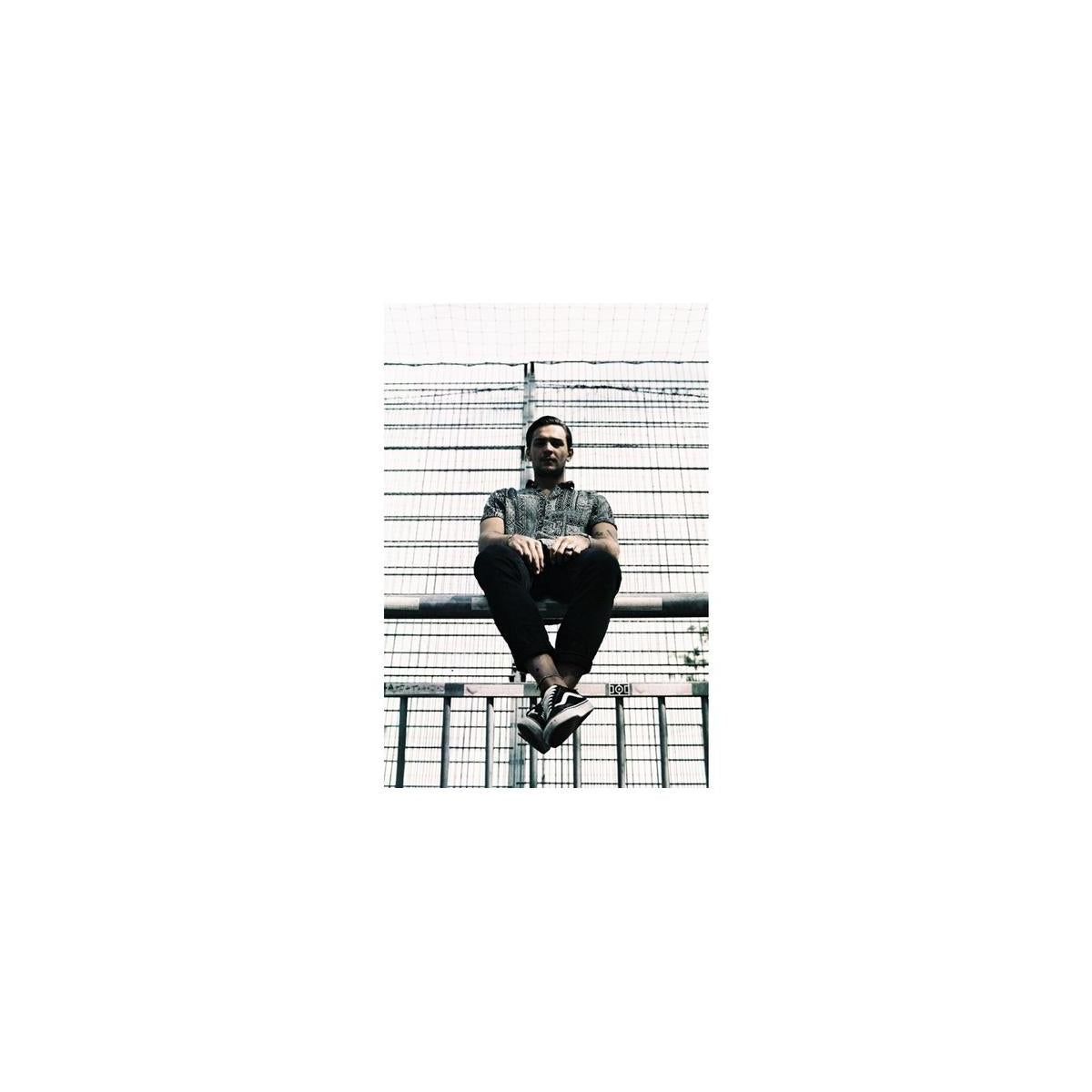 Man sitting on a metal fence, captured with high-contrast, muted tones typical of LomoChrome Metropolis 35mm film.