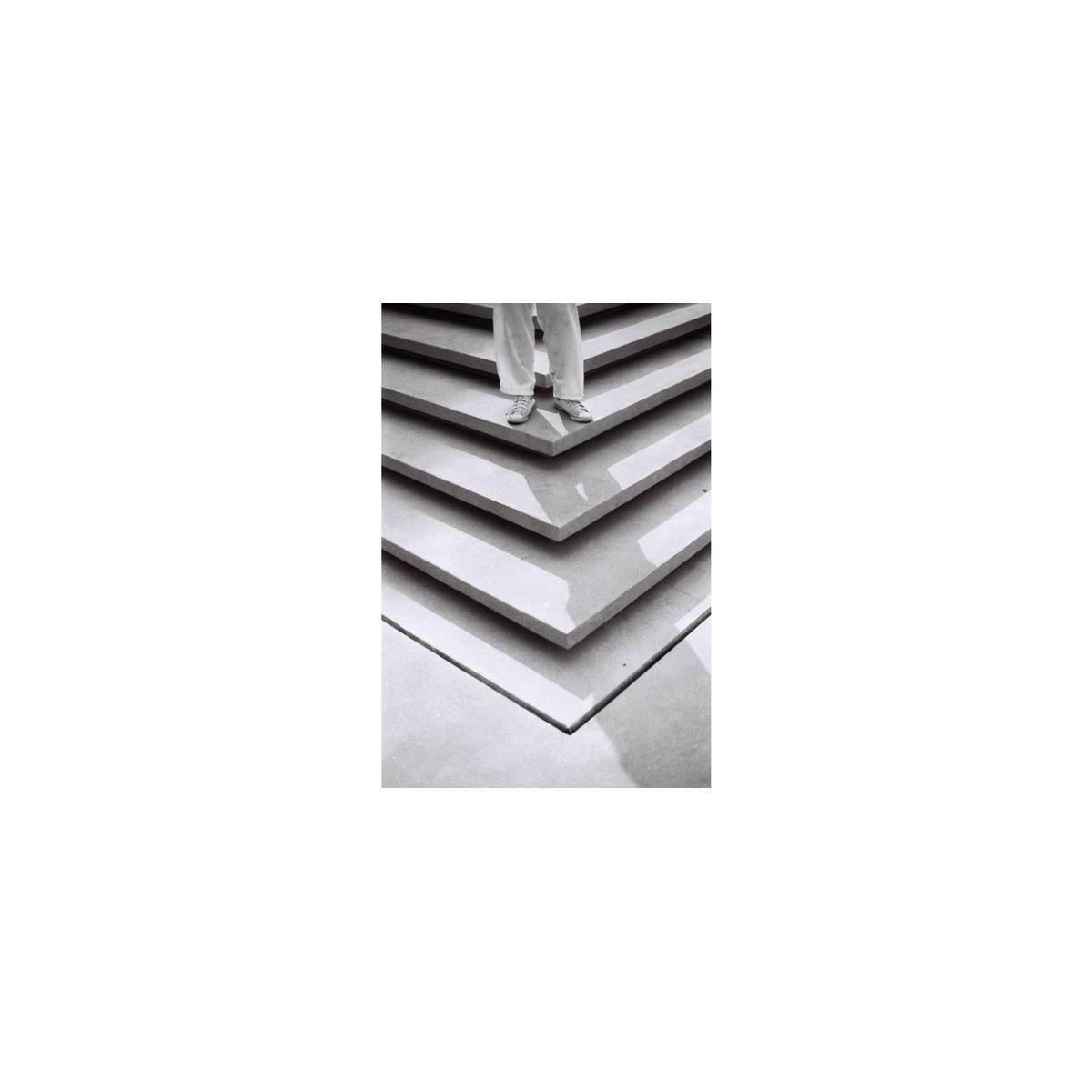 Person standing on geometric concrete steps in a high-contrast black and white photograph with fine grain.
