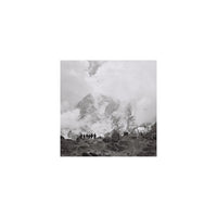 Black and white square-format film shot of a group of hikers standing before a cloudy, snow-capped mountain peak.