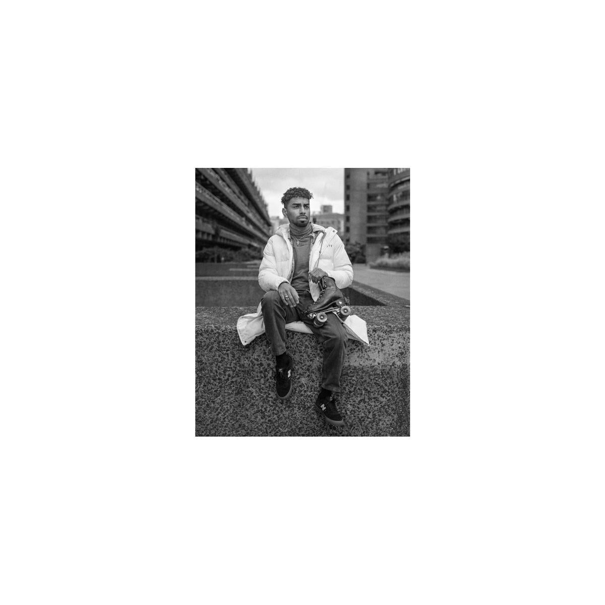 Man in a puffer jacket holding roller skates, captured in cinematic black and white on Lomography Berlin Kino 400 film.