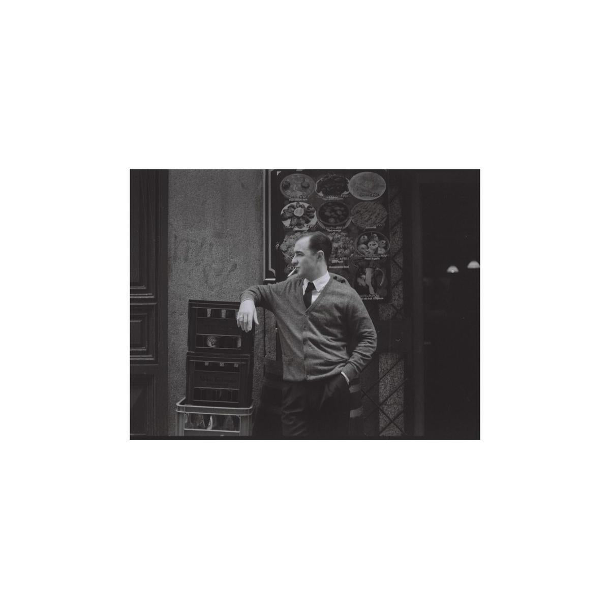 Cinematic black and white portrait of a man leaning against crates, shot on Lomography Berlin Kino 400 120 film.