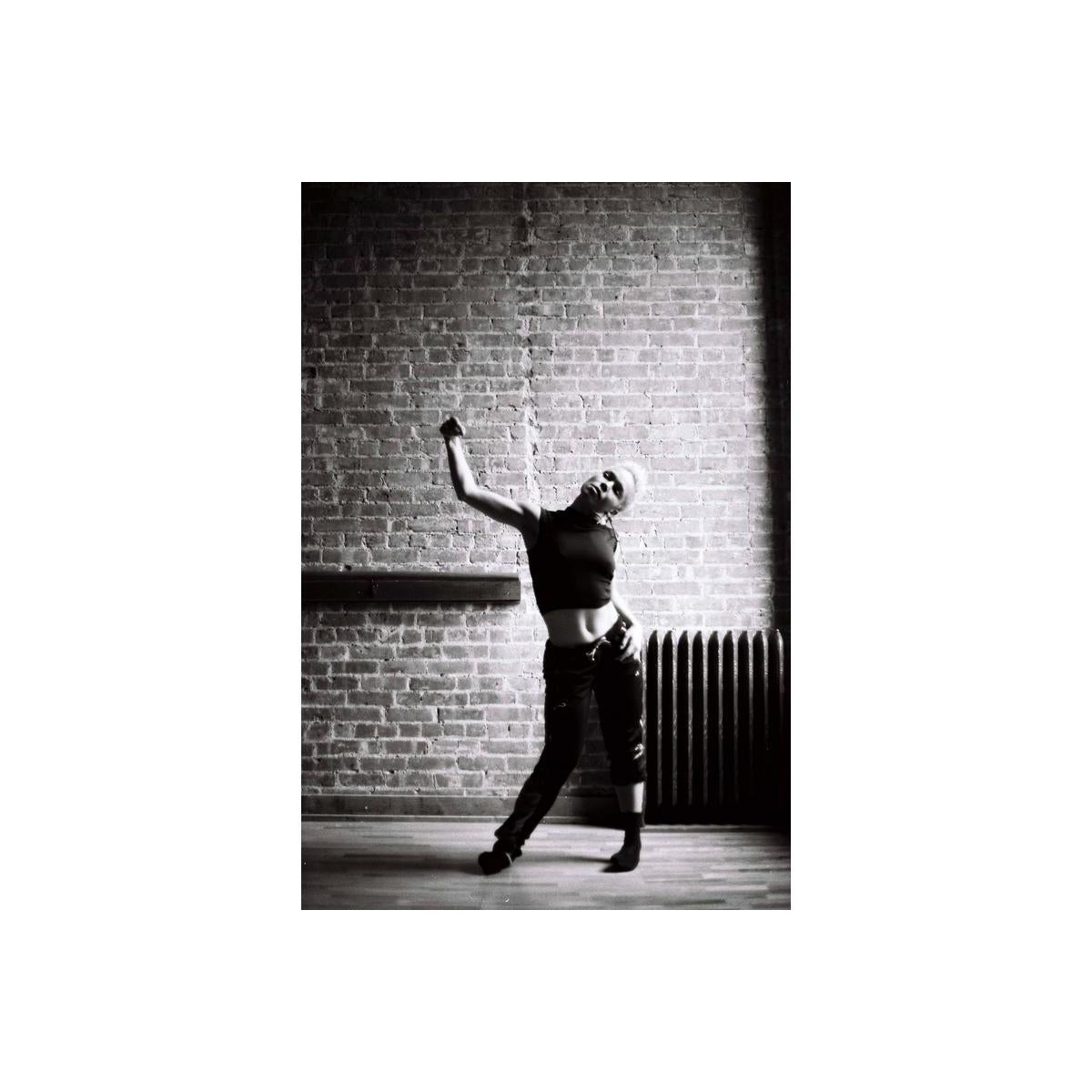 High-contrast black and white portrait of a person posing against a brick wall, shot on Lomography Earl Grey 100 film.