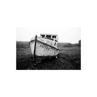High-contrast black and white film shot of an abandoned wooden boat named Edith E resting in a grassy field.
