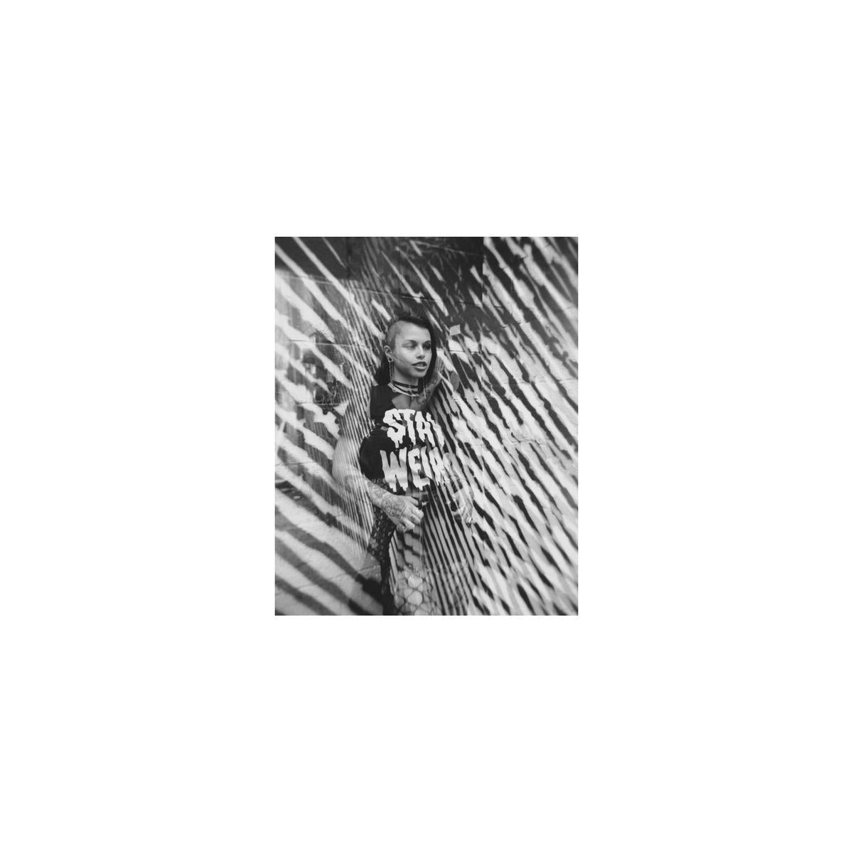 High-contrast black and white portrait of a person wearing a Stay Weird shirt, captured with sharp, fine-grain 35mm film.