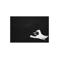 High-contrast black and white portrait of a person in a white shirt lying in dark grass, shot on Lomography Fantome Kino 8.