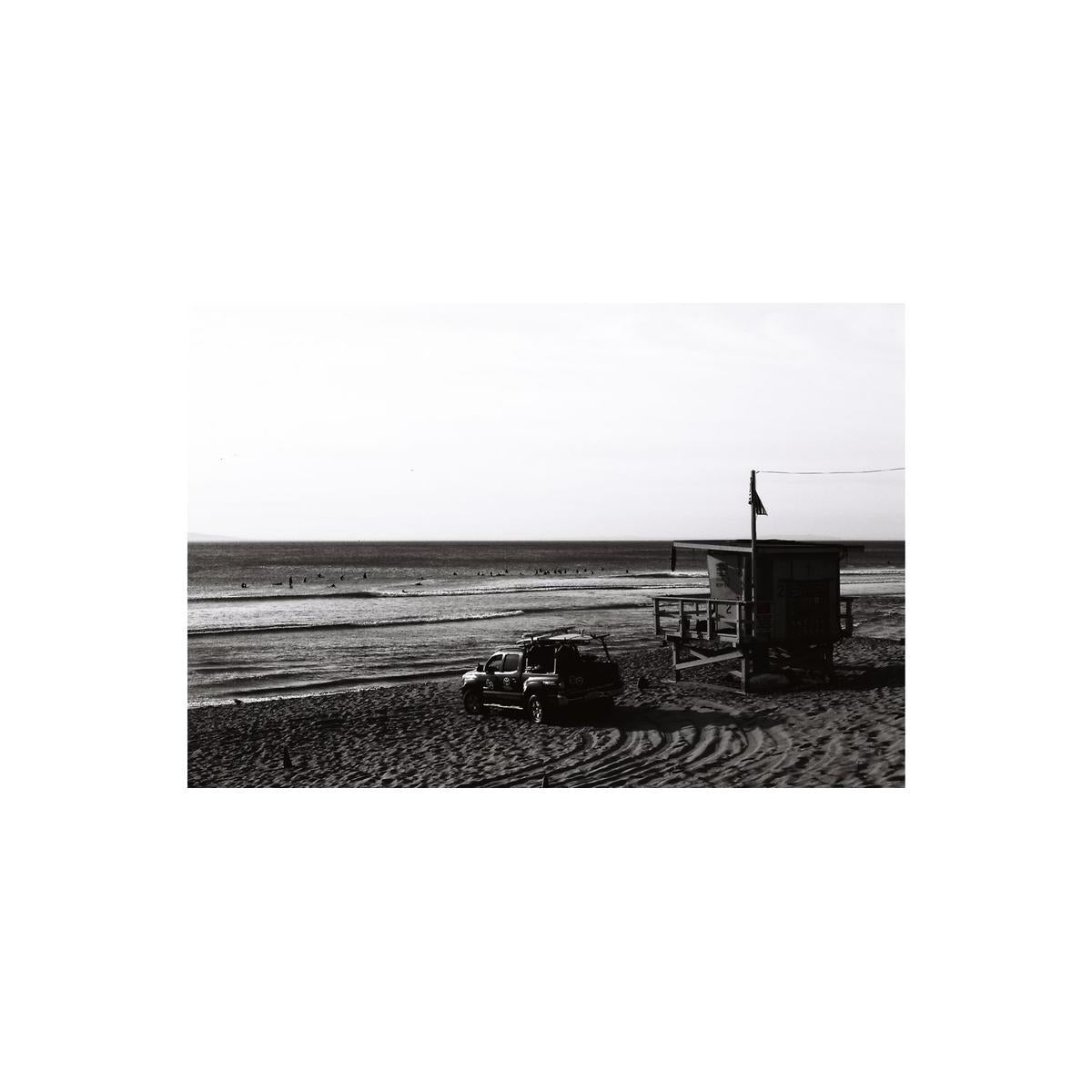 High-contrast black and white beach scene with a lifeguard tower and truck, captured on Lomography Fantome Kino 8 film.