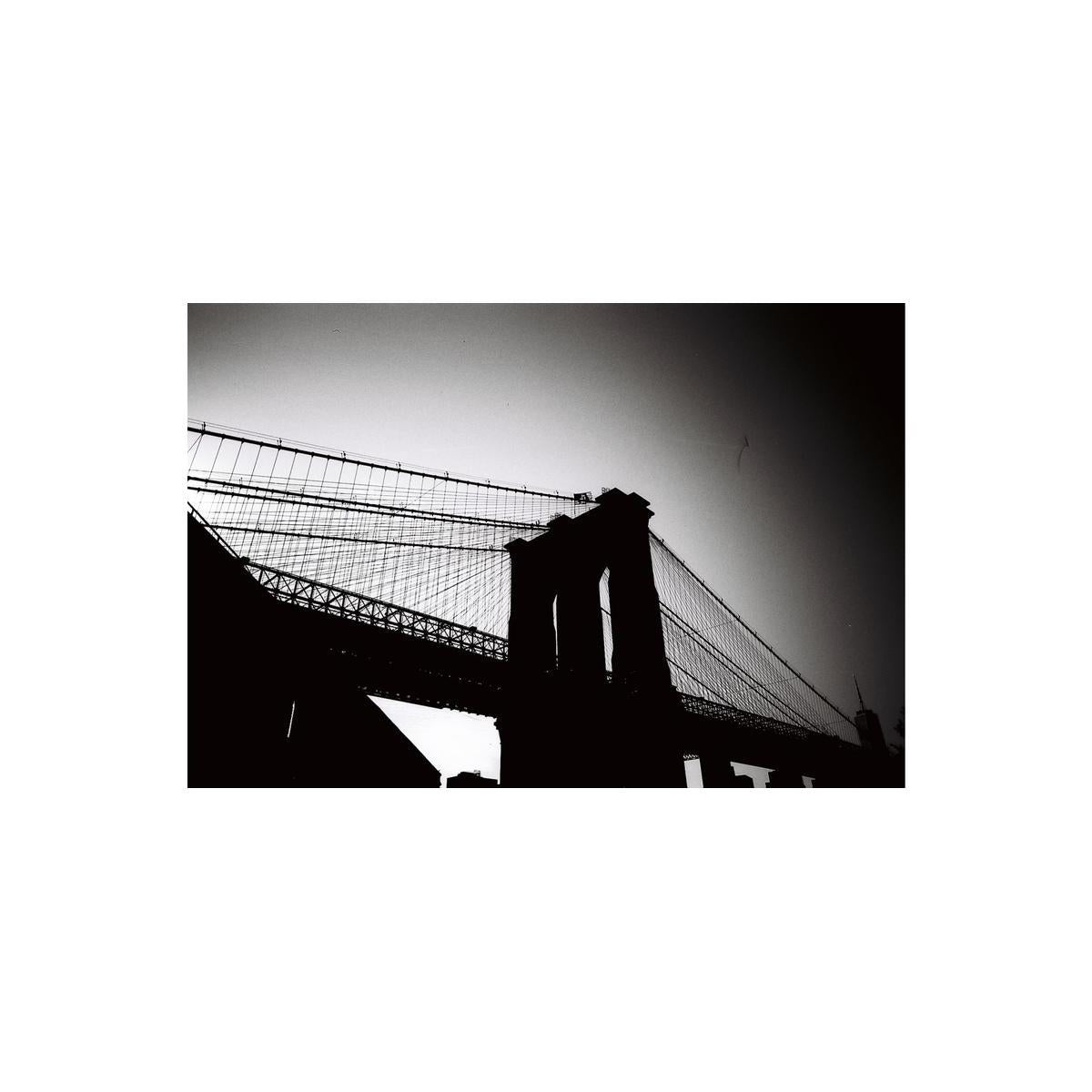 High-contrast black and white photograph of the Brooklyn Bridge silhouette against a bright sky, shot on 35mm film.