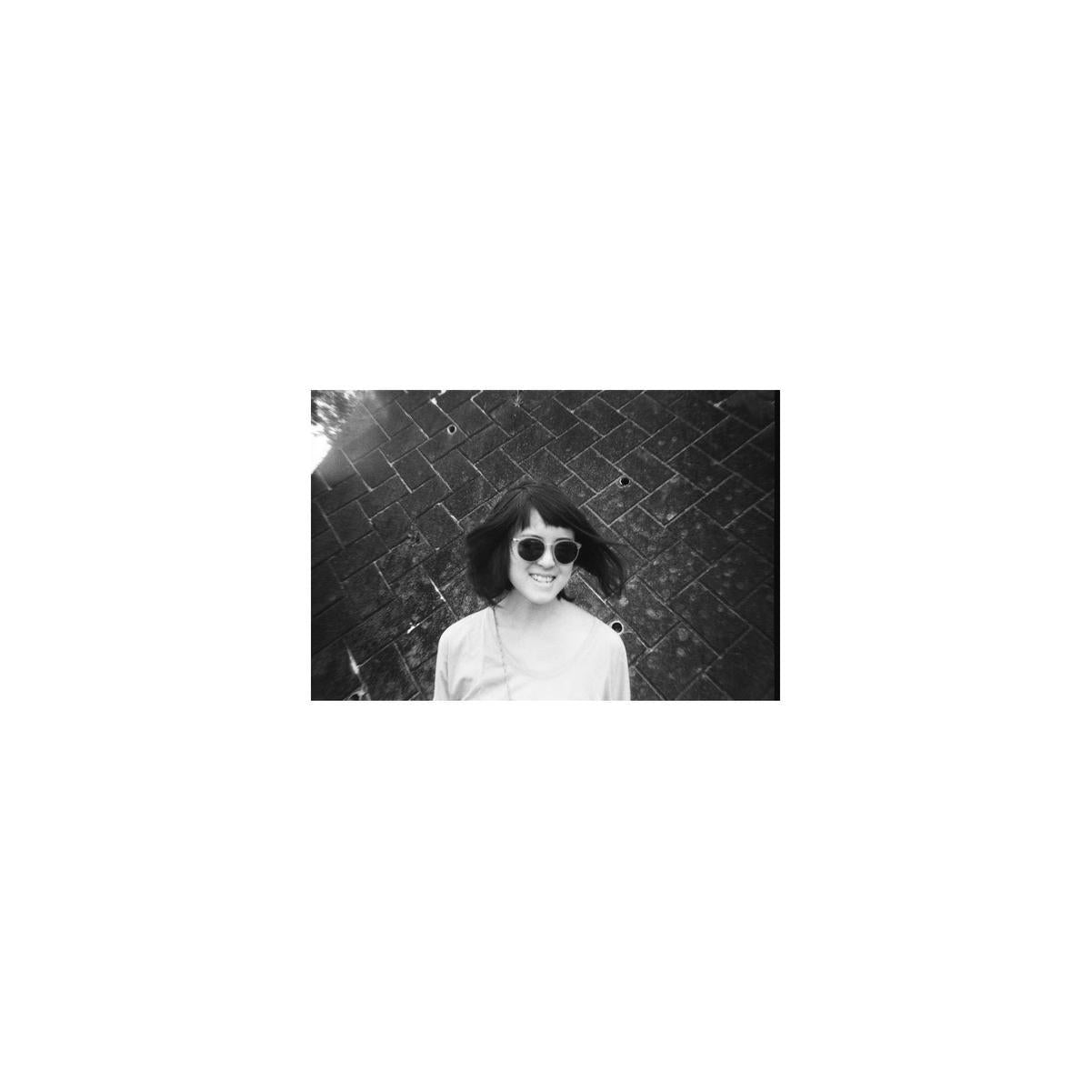 Black and white portrait of a woman in sunglasses against a brick wall, captured on Lomography Lady Grey 400 film.
