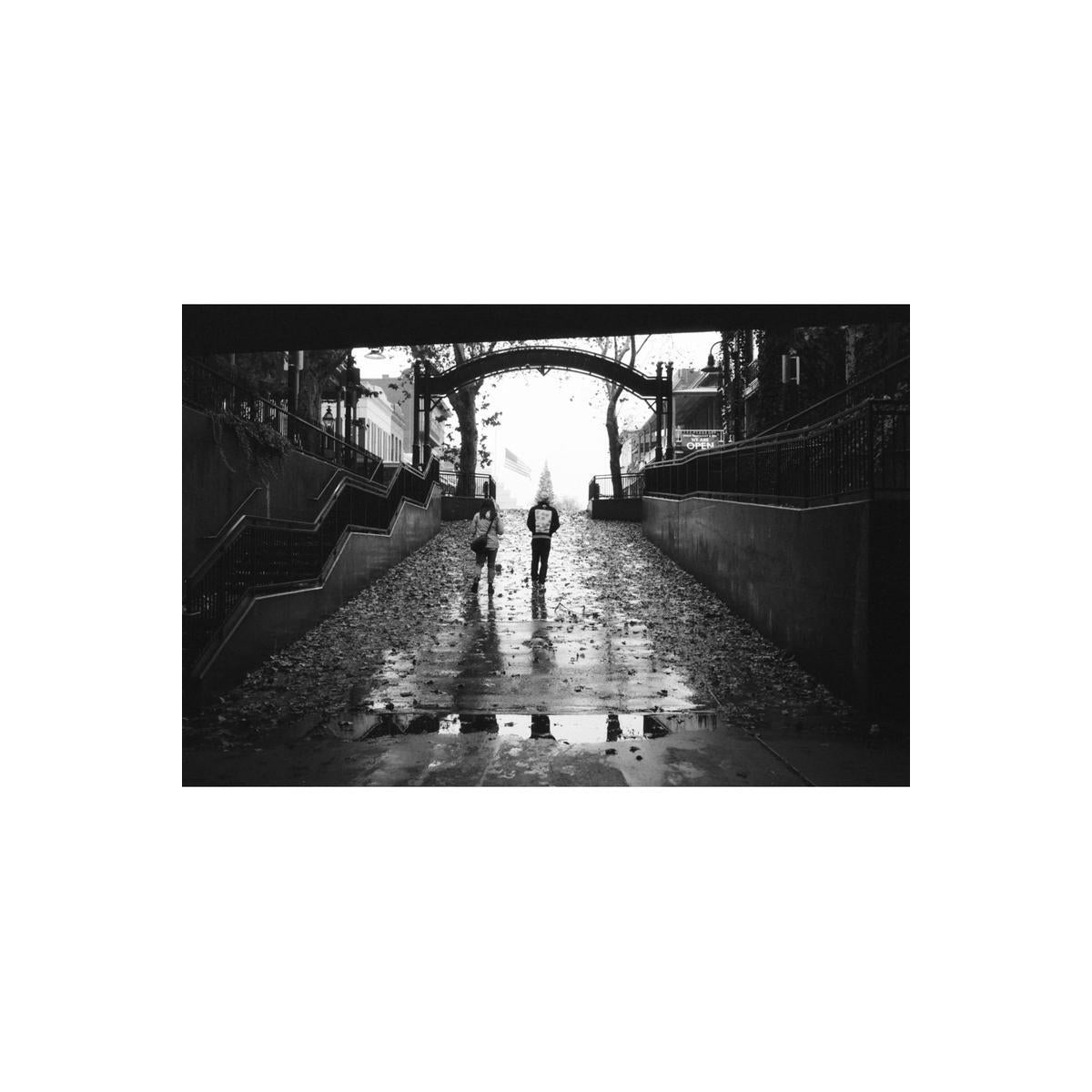 Black and white street photography shot on Lomography Lady Grey 400 film, showing two people walking under an archway.