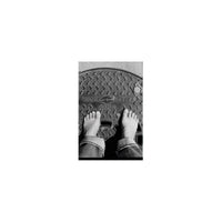 Bare feet standing on a textured metal manhole cover, captured in high-contrast black and white 35mm film.