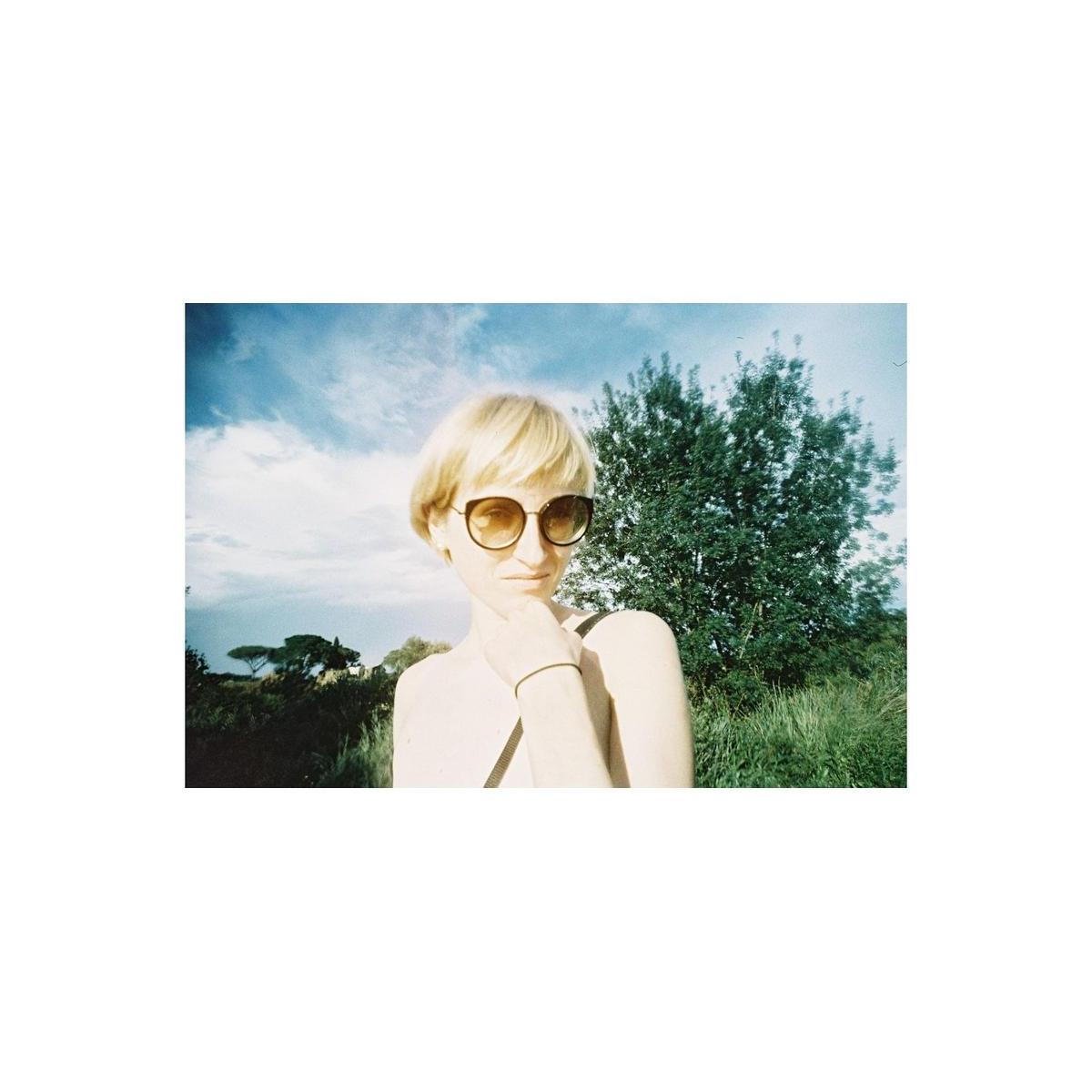 Portrait of a woman wearing sunglasses, captured with Lomography Metropolis film featuring muted tones and high contrast.