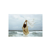 Person standing on a beach holding a white cloth, captured with the muted, high-contrast aesthetic of Lomography Metropolis.