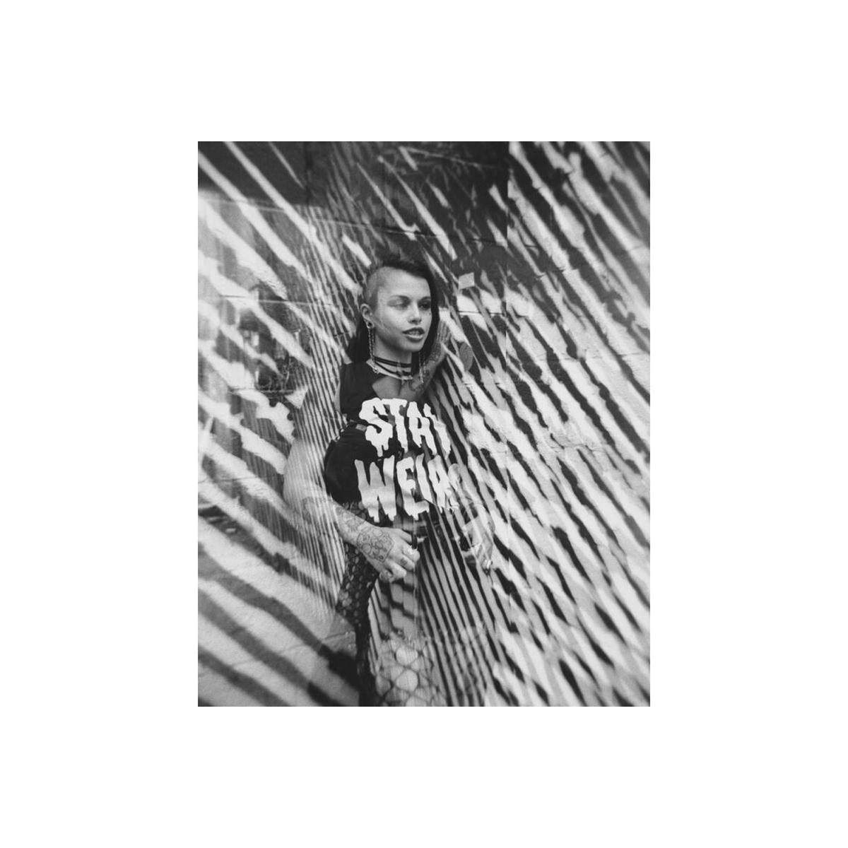 Black and white portrait of a person wearing a Stay Weird shirt, captured with high-contrast shadows and fine grain film.